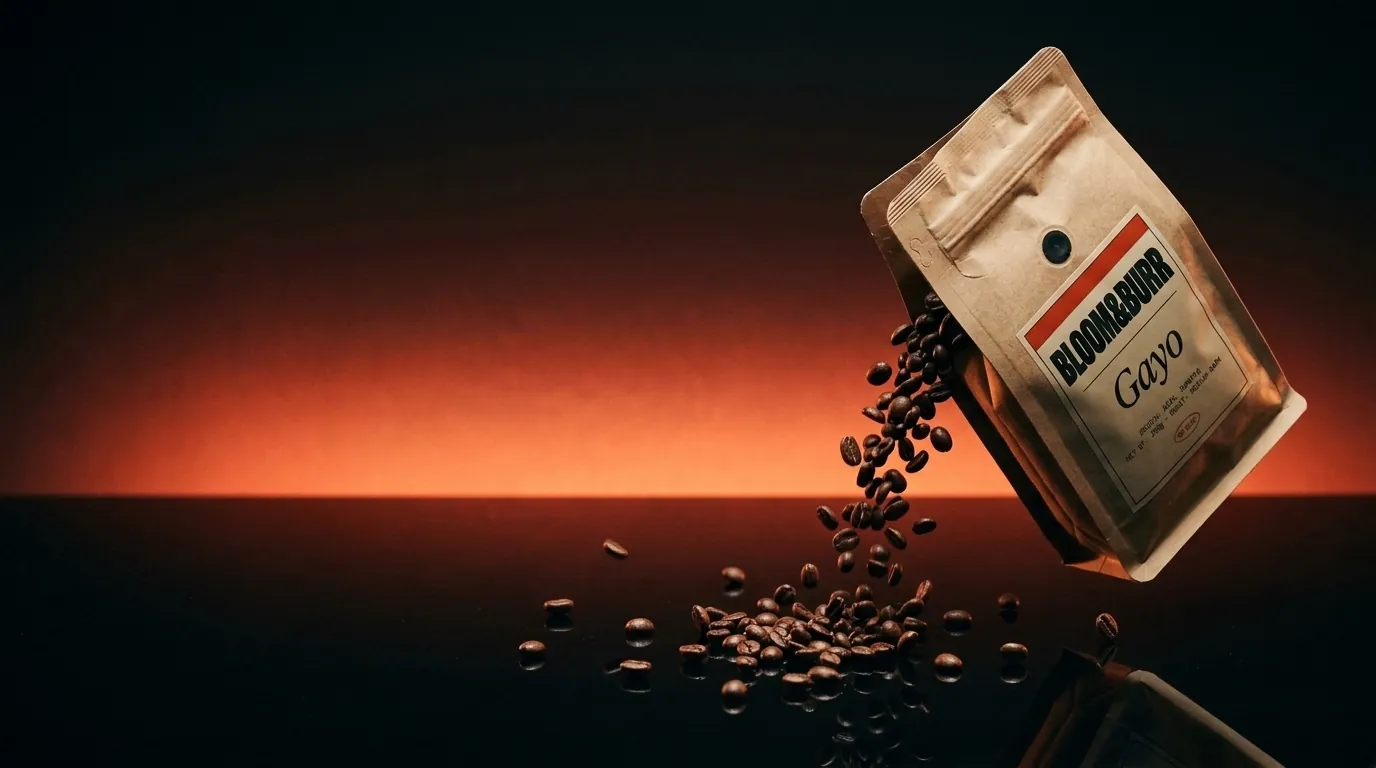 A Gayo pouch tipped over in a dark studio, roasted beans pouring onto a glossy floor