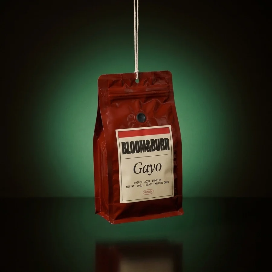A cherry-red Gayo pouch hanging from a cotton string in a green glow over a dark glossy floor