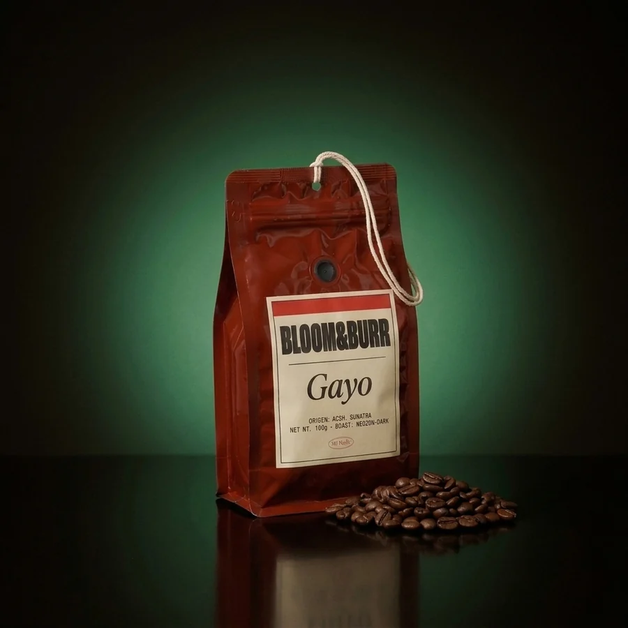 The Gayo pouch standing on the glossy floor in the same glow, a heap of roasted beans beside it