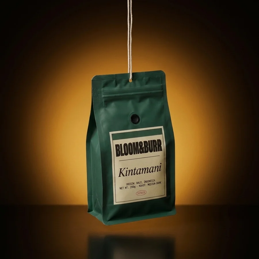 A coffee-leaf green Kintamani pouch hanging from a cotton string in an amber glow over a dark glossy floor